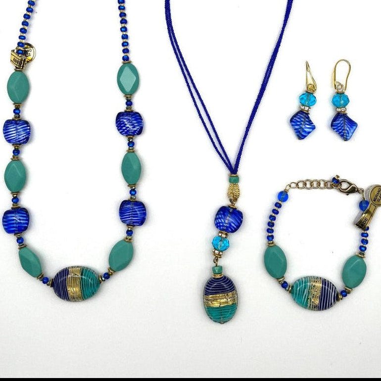 A jewelry set featuring a long beaded necklace, a matching pendant necklace, a bracelet, and a pair of drop earrings. The pieces feature vibrant royal blue beads, turquoise green beads, and antique gold-toned metal accents, arranged neatly on a plain white background.